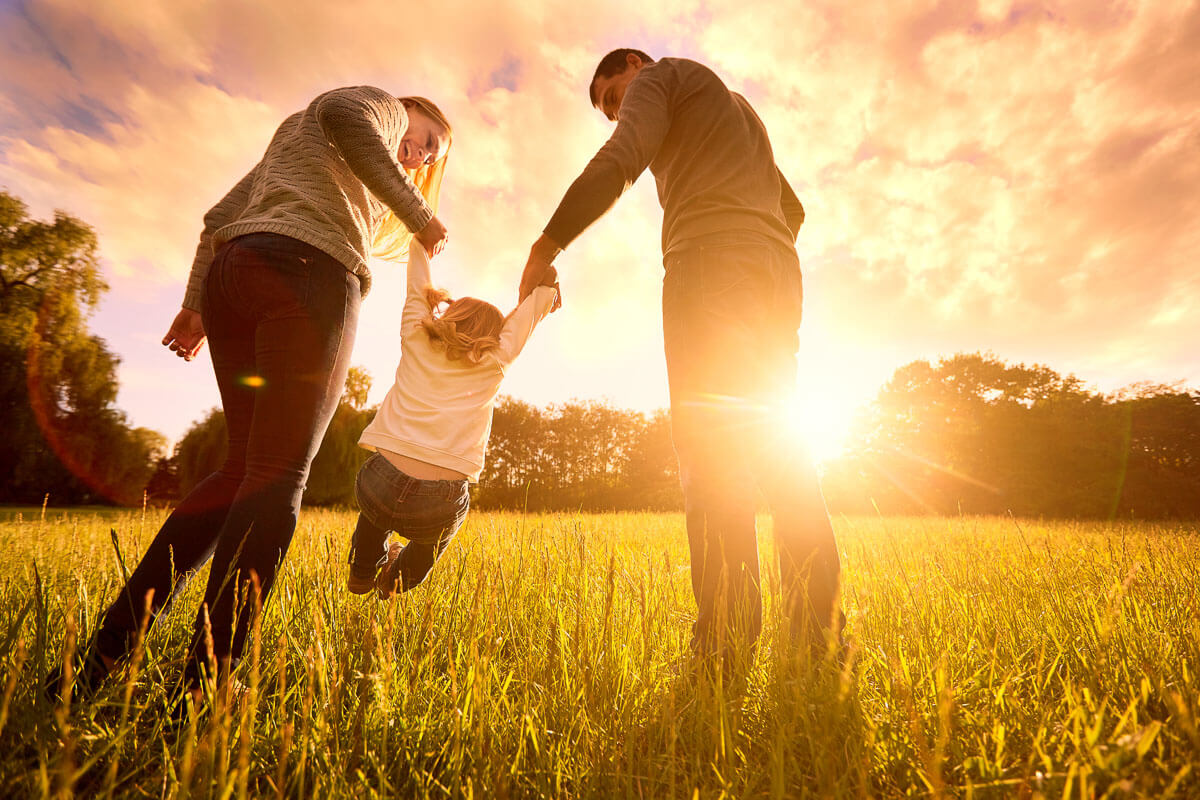 Family in a park at sunset, with two adults swinging the child between them.