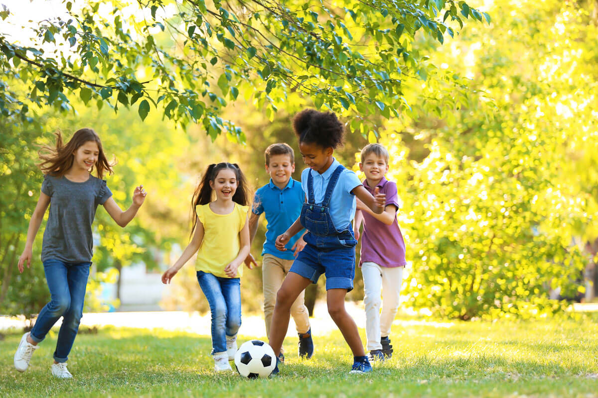 Diverse group of five children playing football in a park