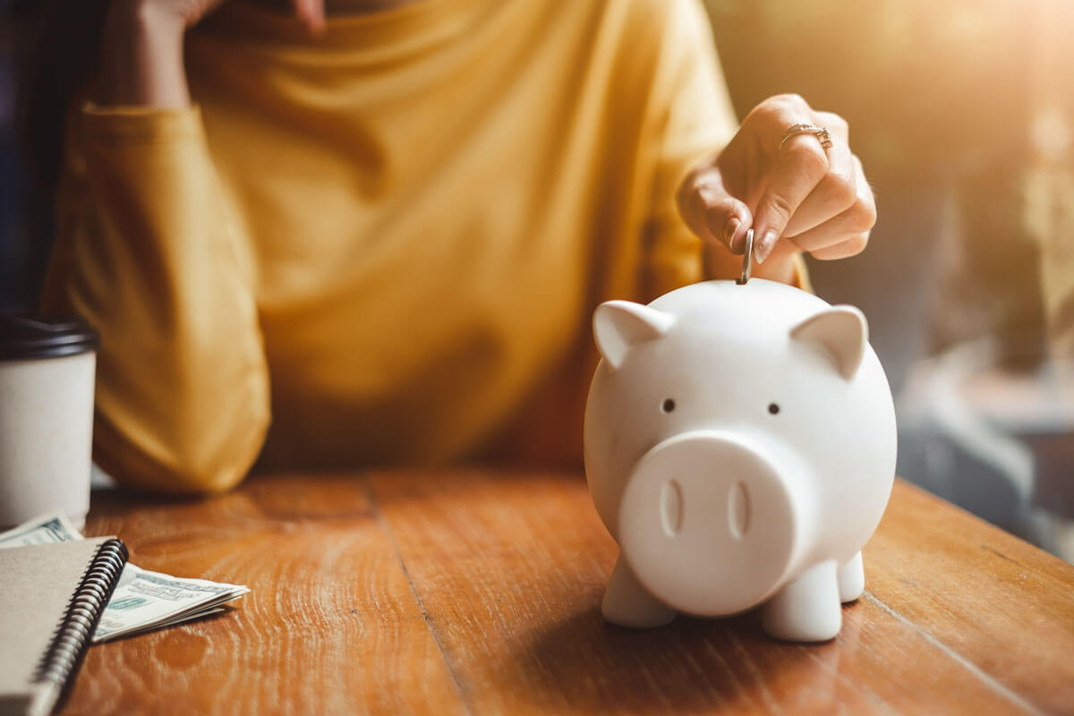 Woman in yellow sweater putting coins into a white piggy bank.
