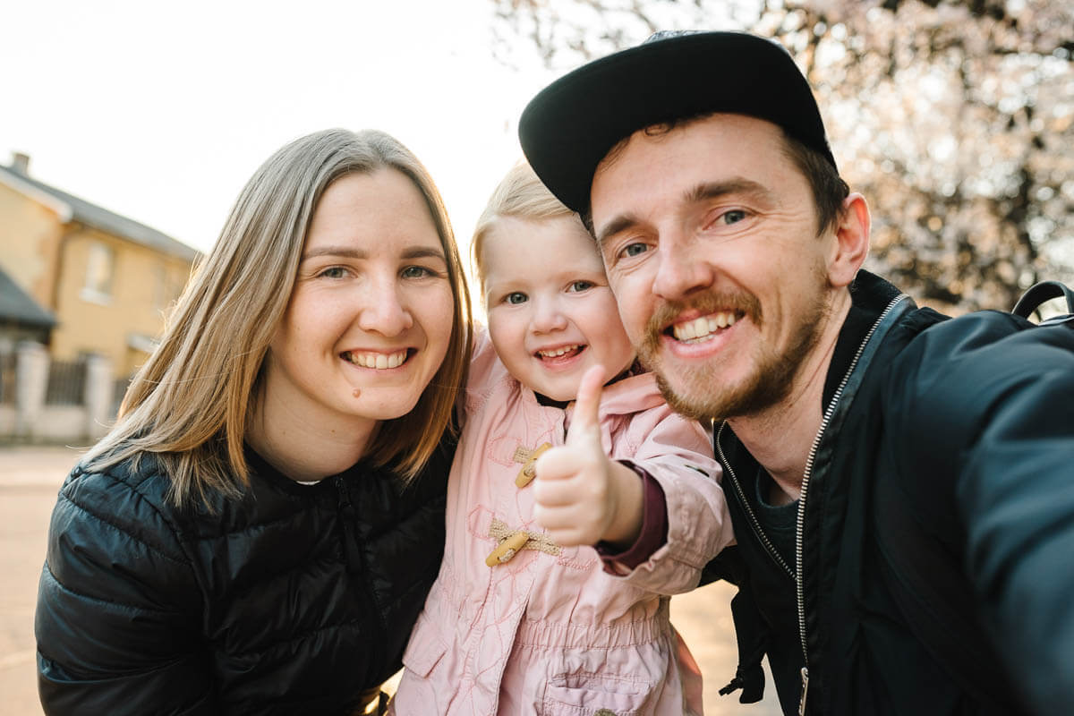 A family of three in the street crouching to take a selfie while the child is giving the thumbs up