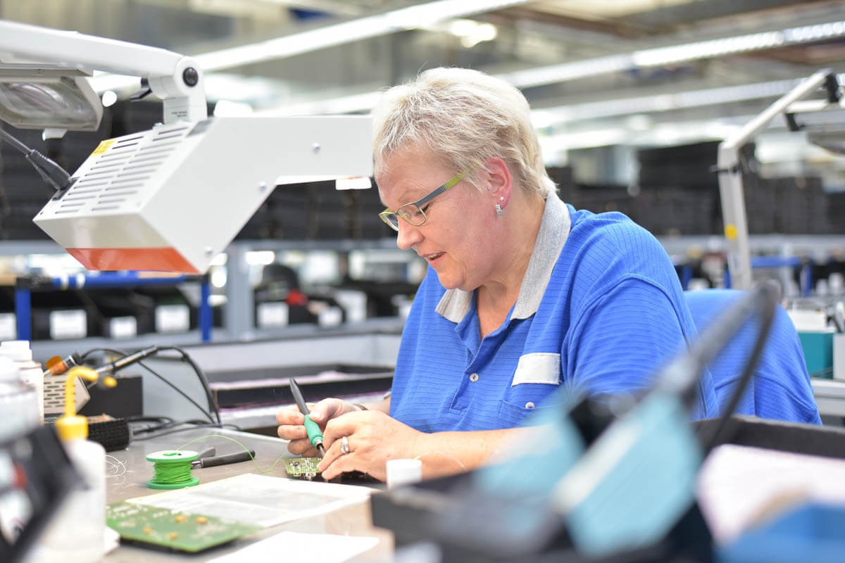 A person working in a factory concentrating on soldering a chip onto a board
