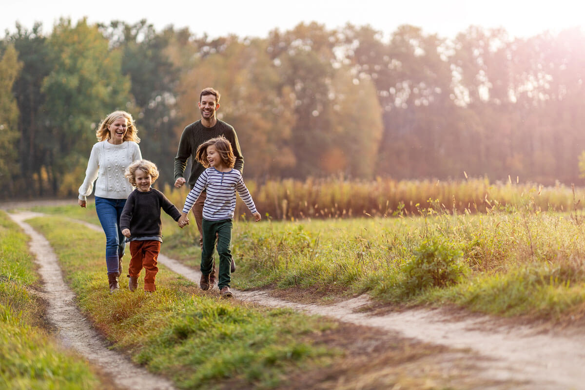 Family of four walking along a country track as the sun is starting to set, with two adults are smiling while two young children hold hands.