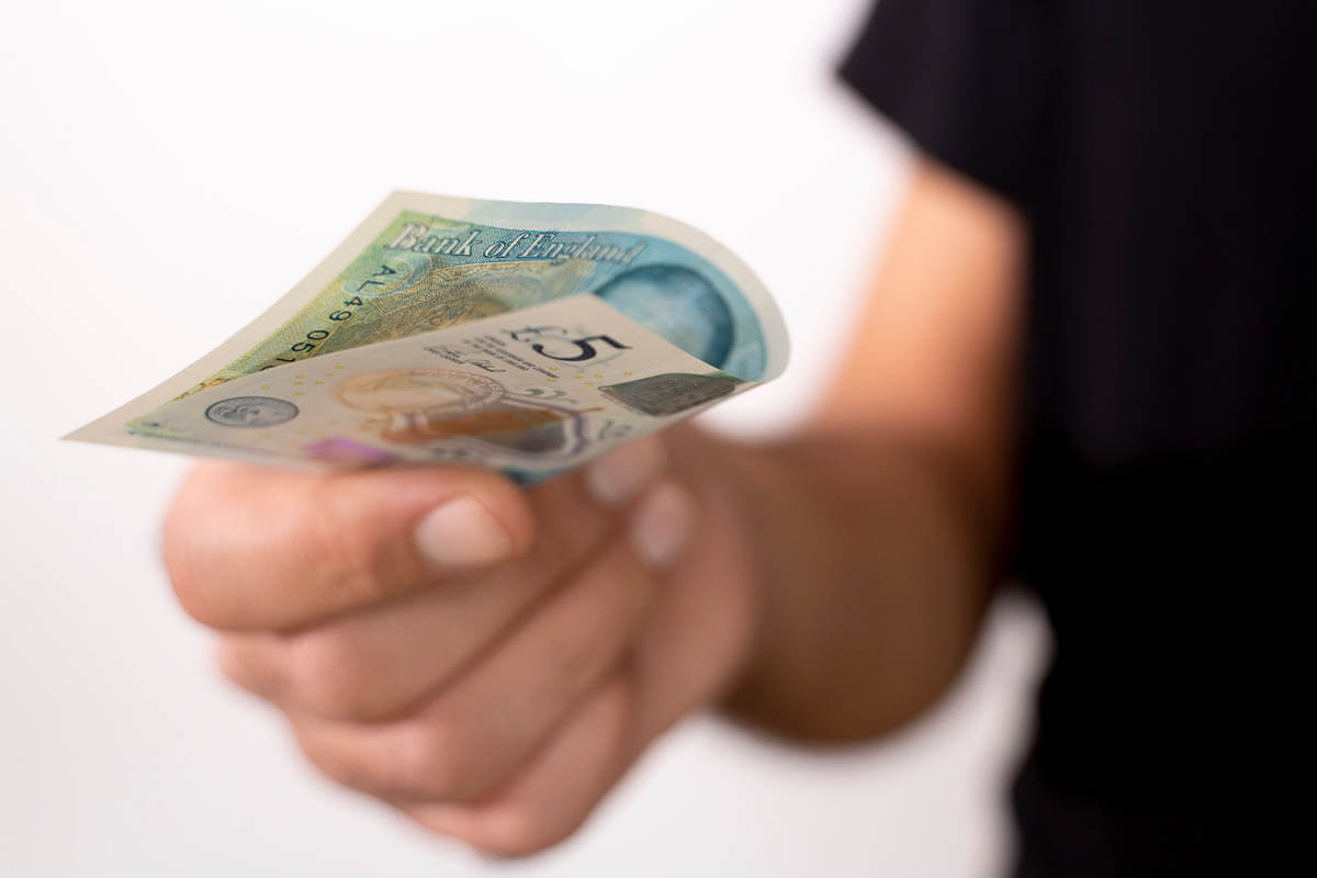 A person holding out a folded £5 note